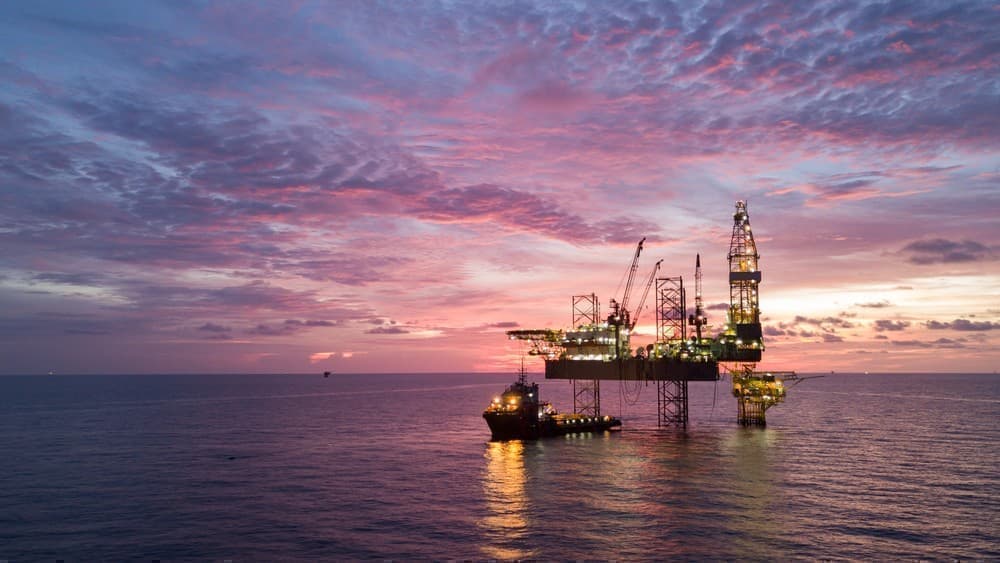 Offshore oil platform at sunset with drilling equipment and support vessel